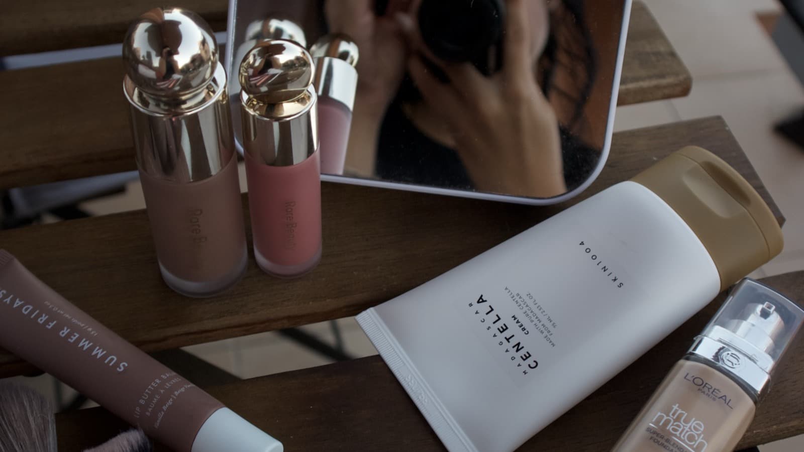 Skincare and fragrance products on a bench beside a mirror