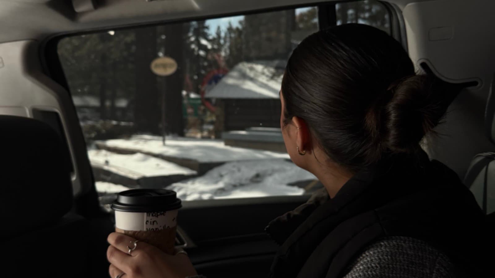 Woman looking out of a car window with a coffee, deep in thought