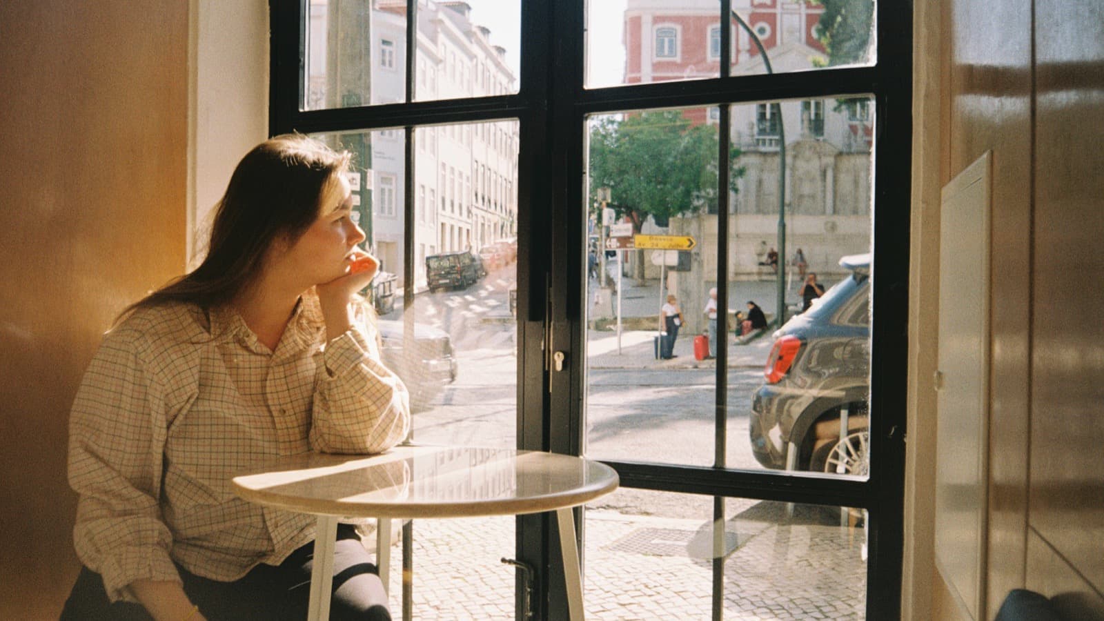 Person sitting by a window deep in thought, reflecting on self-doubt
